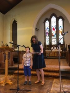 A woman and a boy stand at microphones by the altar of a church, reading during a service.