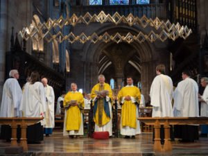 Clergy in yellow and white vestments stand at the altar of a cathedral during an ordination service.
