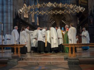 A bishop lays hands on kneeling ordinands at the altar of a cathedral during an ordination service.