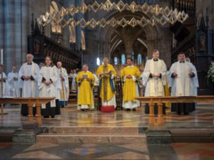 Clergy in yellow and white vestments gather at the altar of a cathedral during an ordination service.