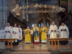 Clergy in yellow and white vestments stand at the altar of a cathedral during an ordination service.