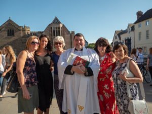 A priest in white robes stands with five women outside Hereford Cathedral.