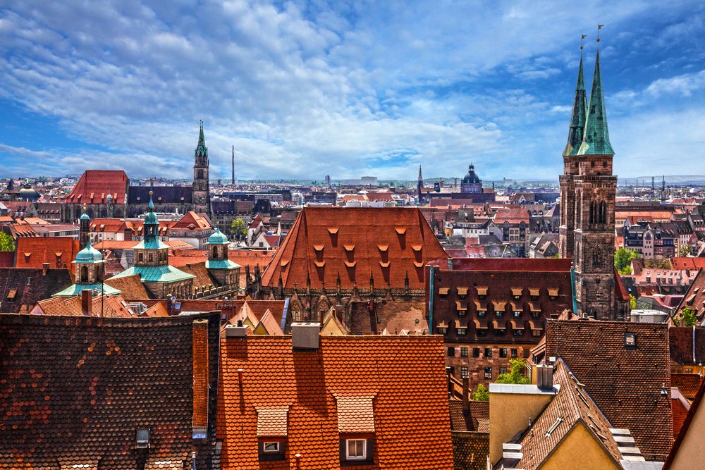 Aerial view of Nuremberg, Germany, with red-tiled rooftops and church spires under a blue sky.