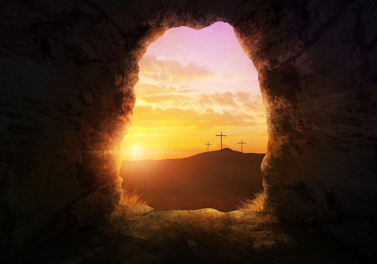 An empty tomb entrance at sunrise, with three crosses silhouetted on a hill beyond, an Easter image.