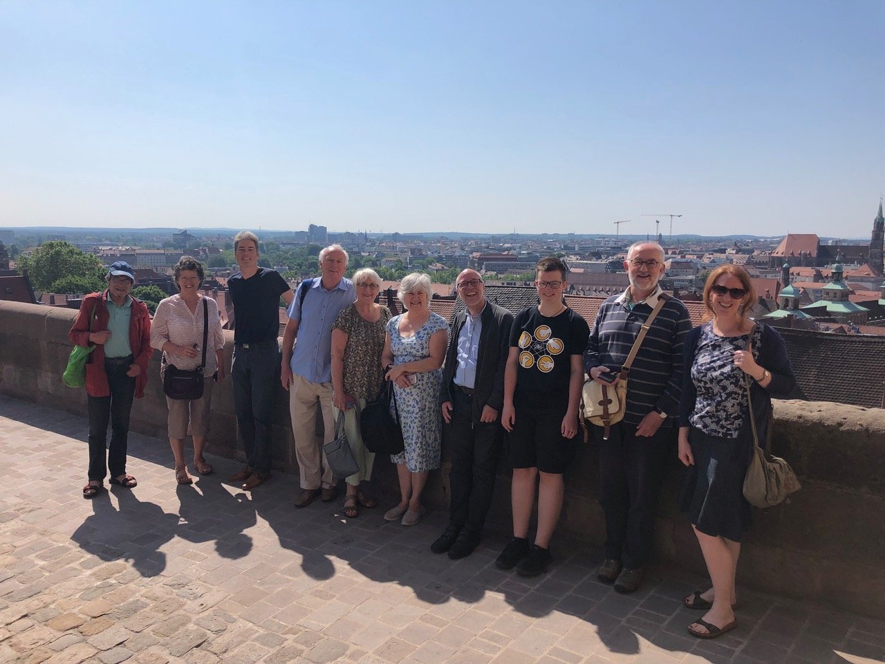 A group of visitors pose together on a city wall overlooking rooftops on a sunny day.