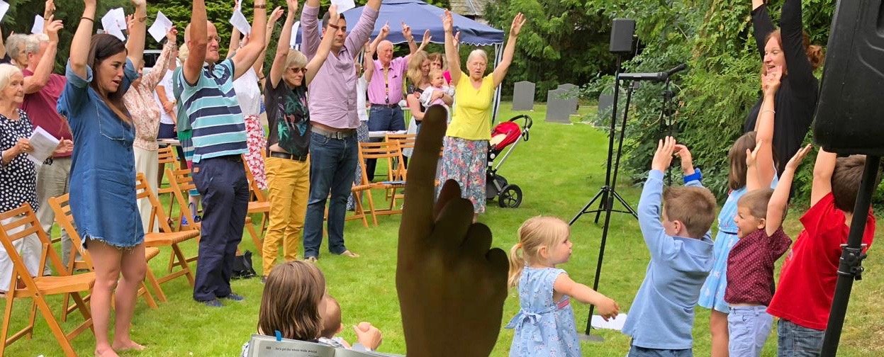 People in a garden raise their hands together during an outdoor worship event.