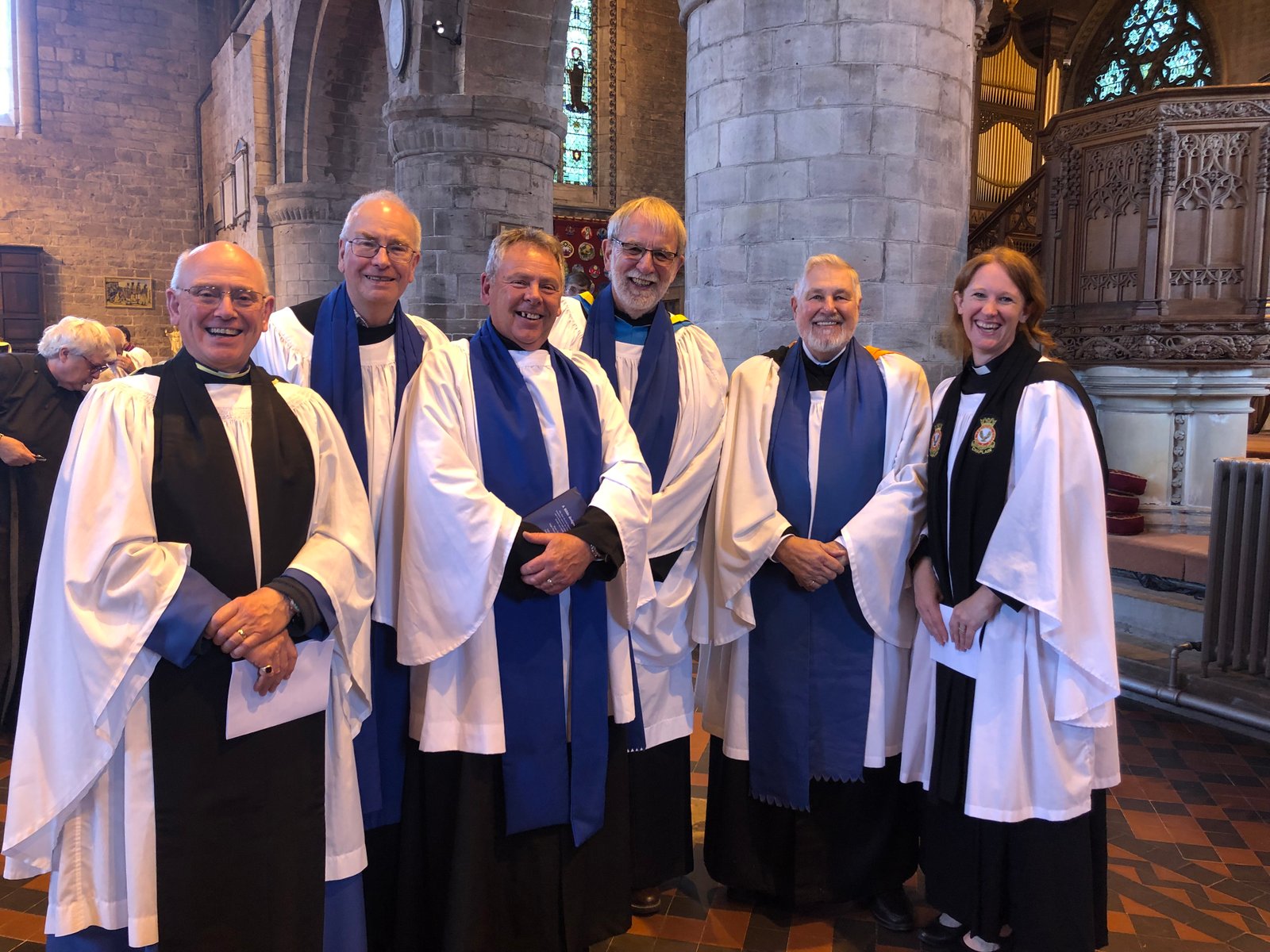 Seven clergy in white and blue robes stand together inside a church.