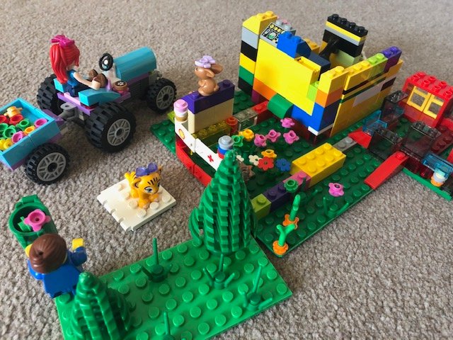 A Lego model of a park scene with a tractor, minifigures, flowers, and a colourful climbing frame.