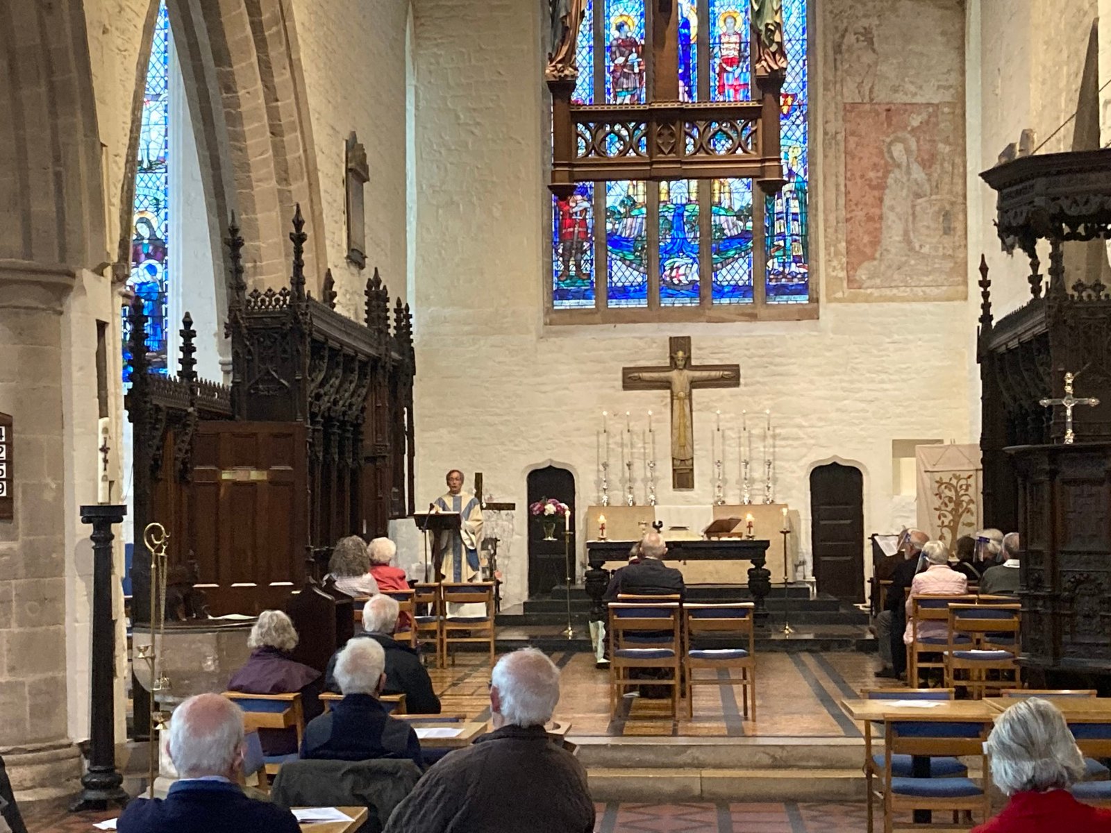 Interior of a church during a service, with the congregation seated facing the altar and a stained glass window above.