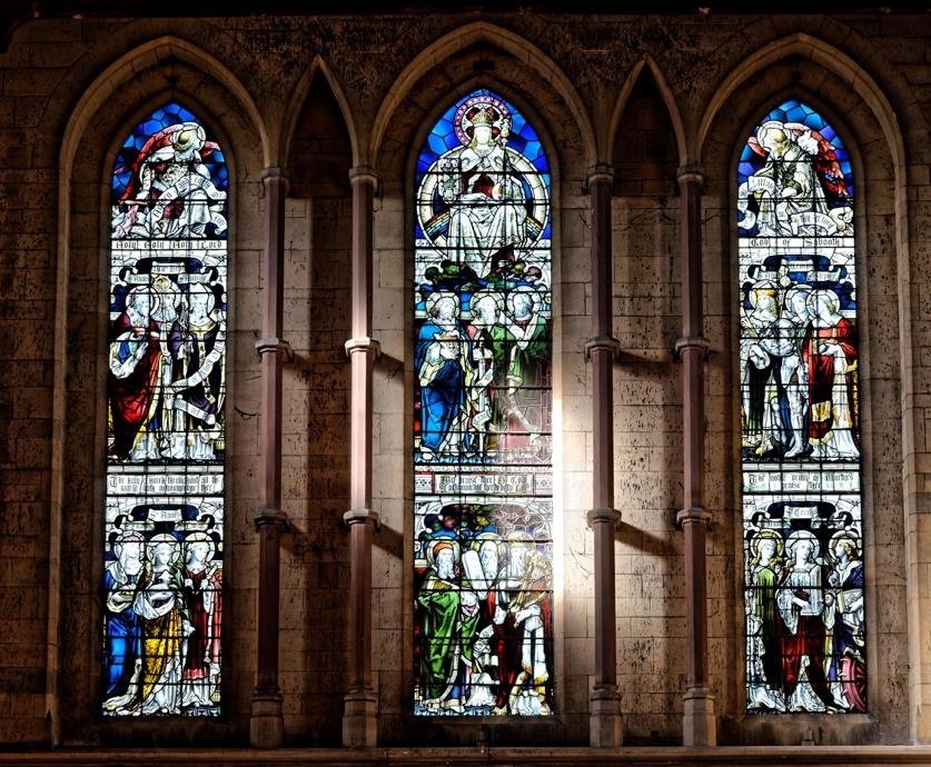 Three tall stained glass windows depicting religious figures, lit from within a church.