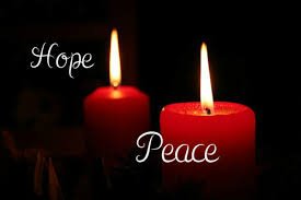 Two red Advent candles, one labeled "Hope" and the other "Peace," lit in darkness.