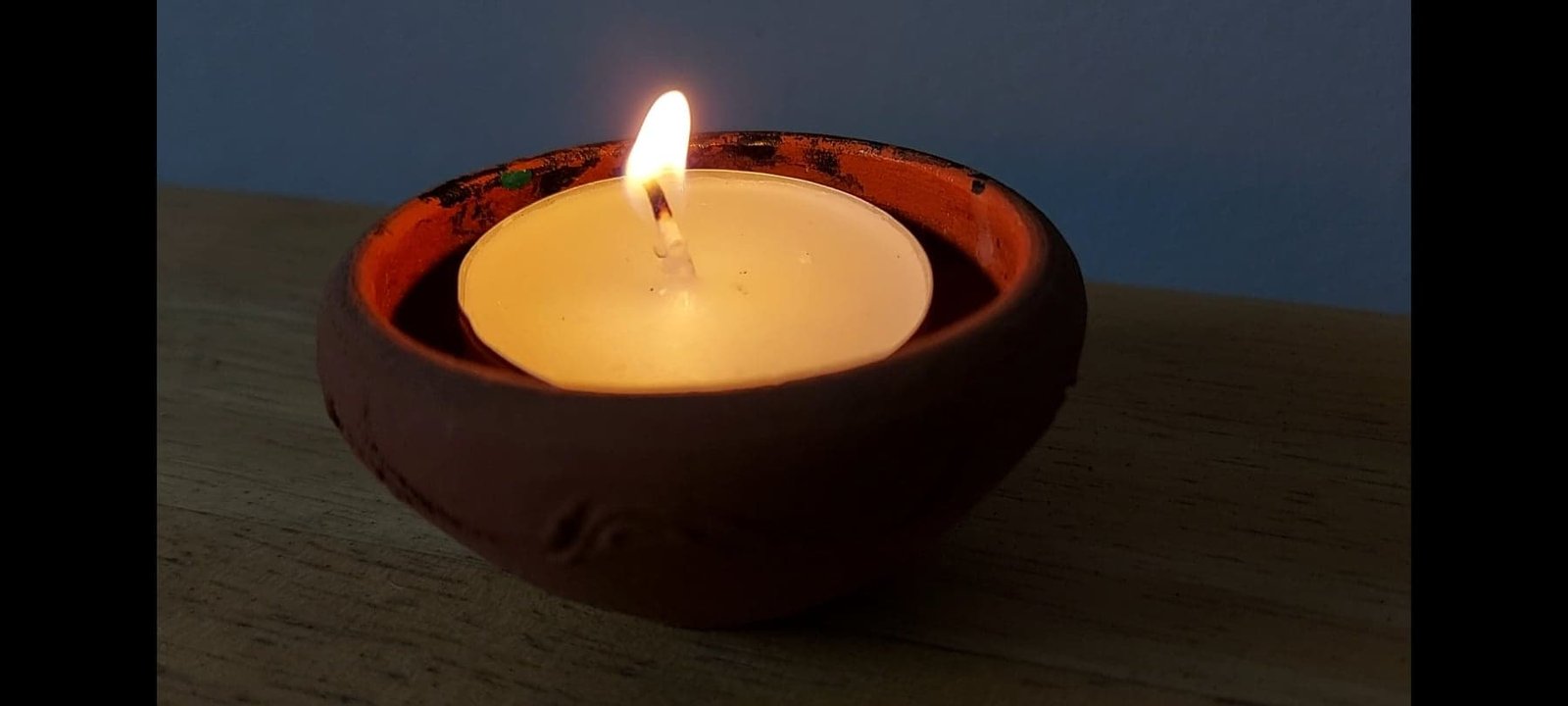 A single candle burning in a small clay bowl on a wooden table.