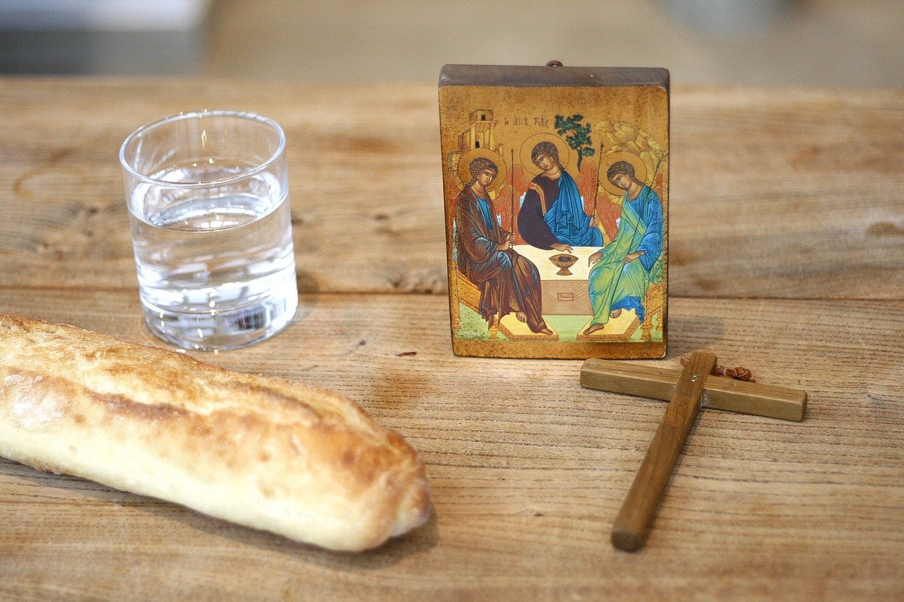 A loaf of bread, a glass of water, a small icon of the Holy Trinity, and a wooden cross arranged on a table, symbolising Lenten fasting.