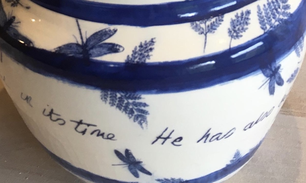 Close-up of a blue and white patterned ceramic vessel with handwritten script and floral decoration.