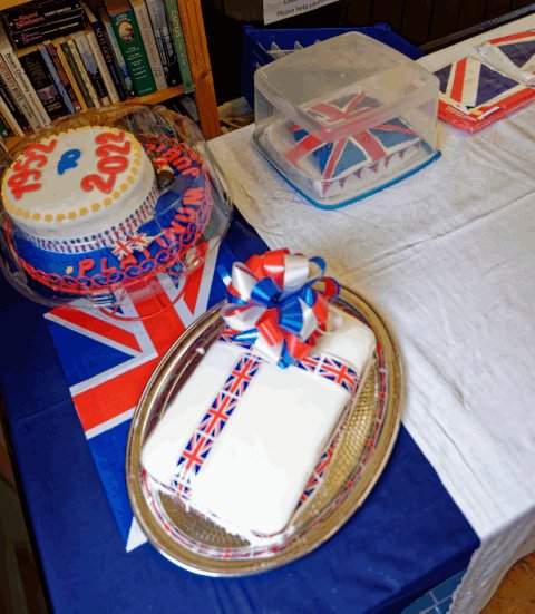A Platinum Jubilee cake decorated with a Union Jack ribbon, displayed on a table with Union Jack flags and bunting.