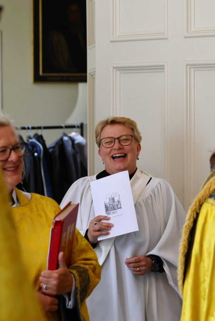Christine Ordained Priest at Hereford Cathedral: woman in clergy robes laughs holding a booklet.