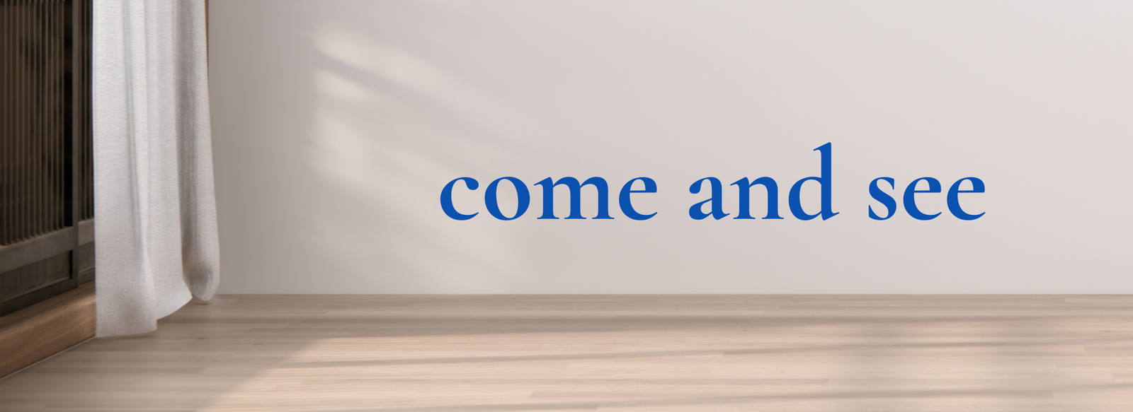 Empty room with wooden floor and white wall featuring blue text "come and see