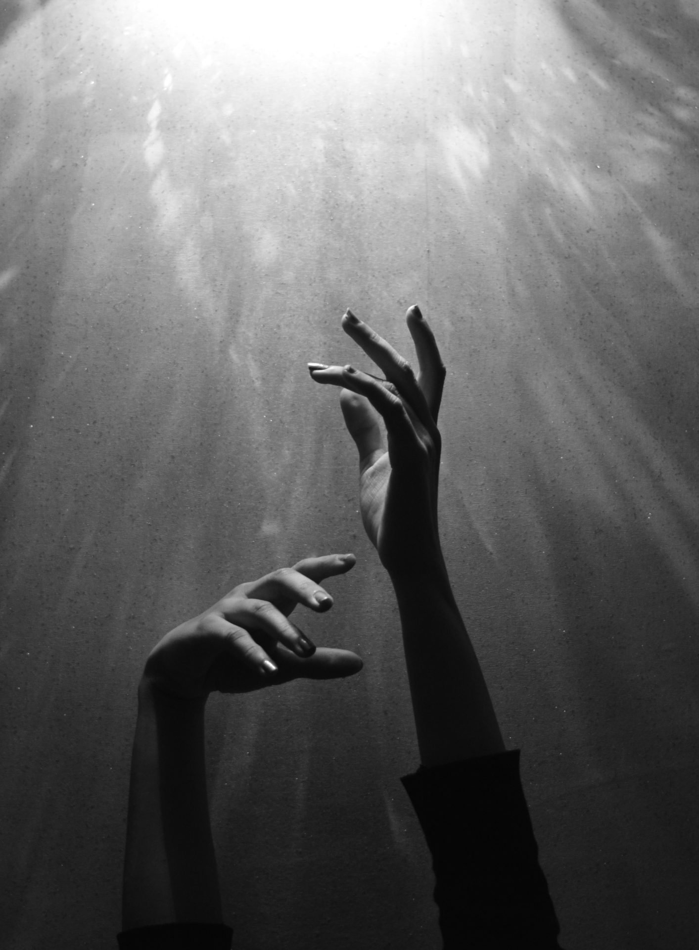 Two hands reaching upwards towards light rays, symbolizing hope and belief.