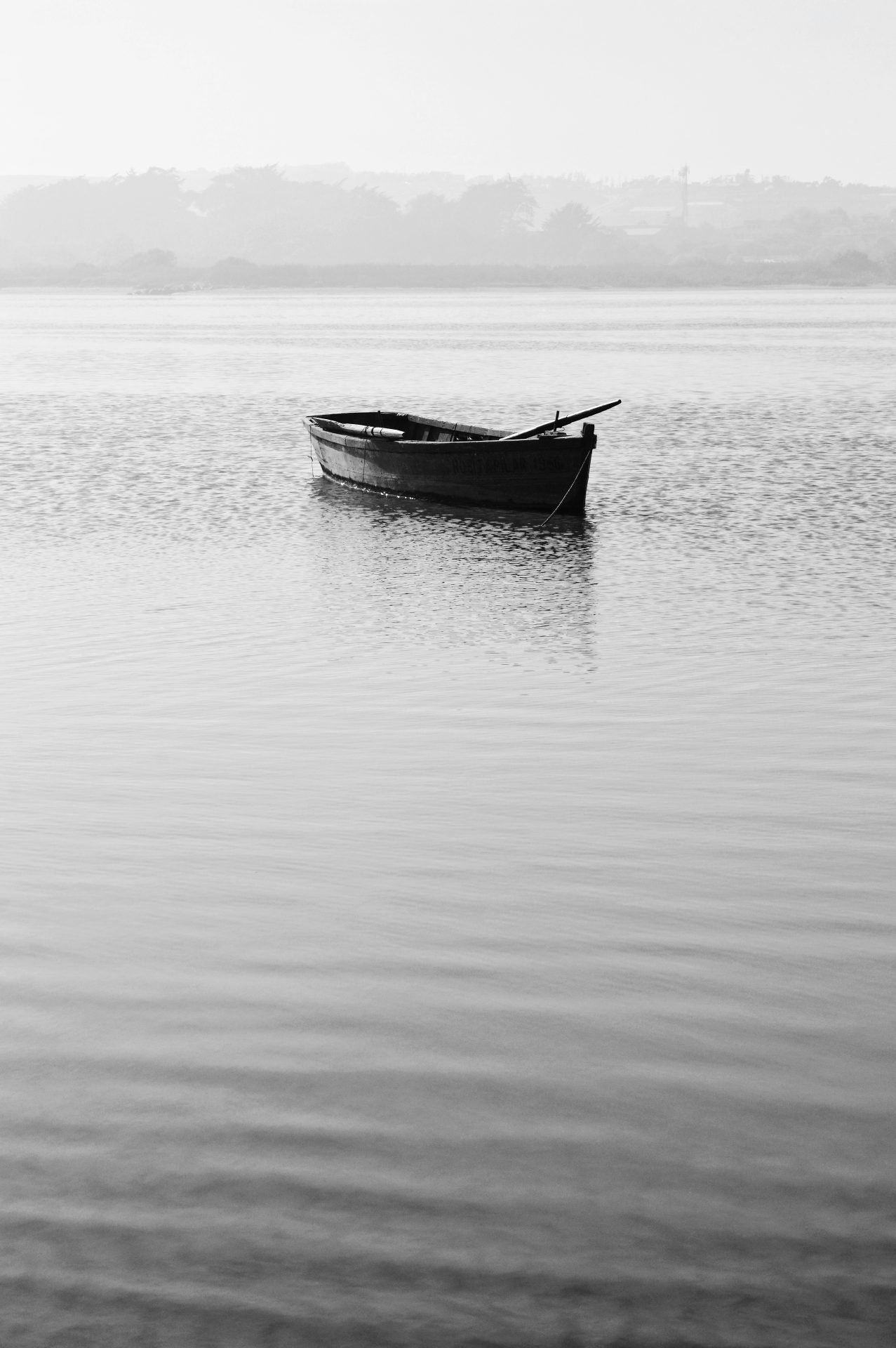 A lone wooden rowboat floats on calm, misty water, reflecting the serene landscape.