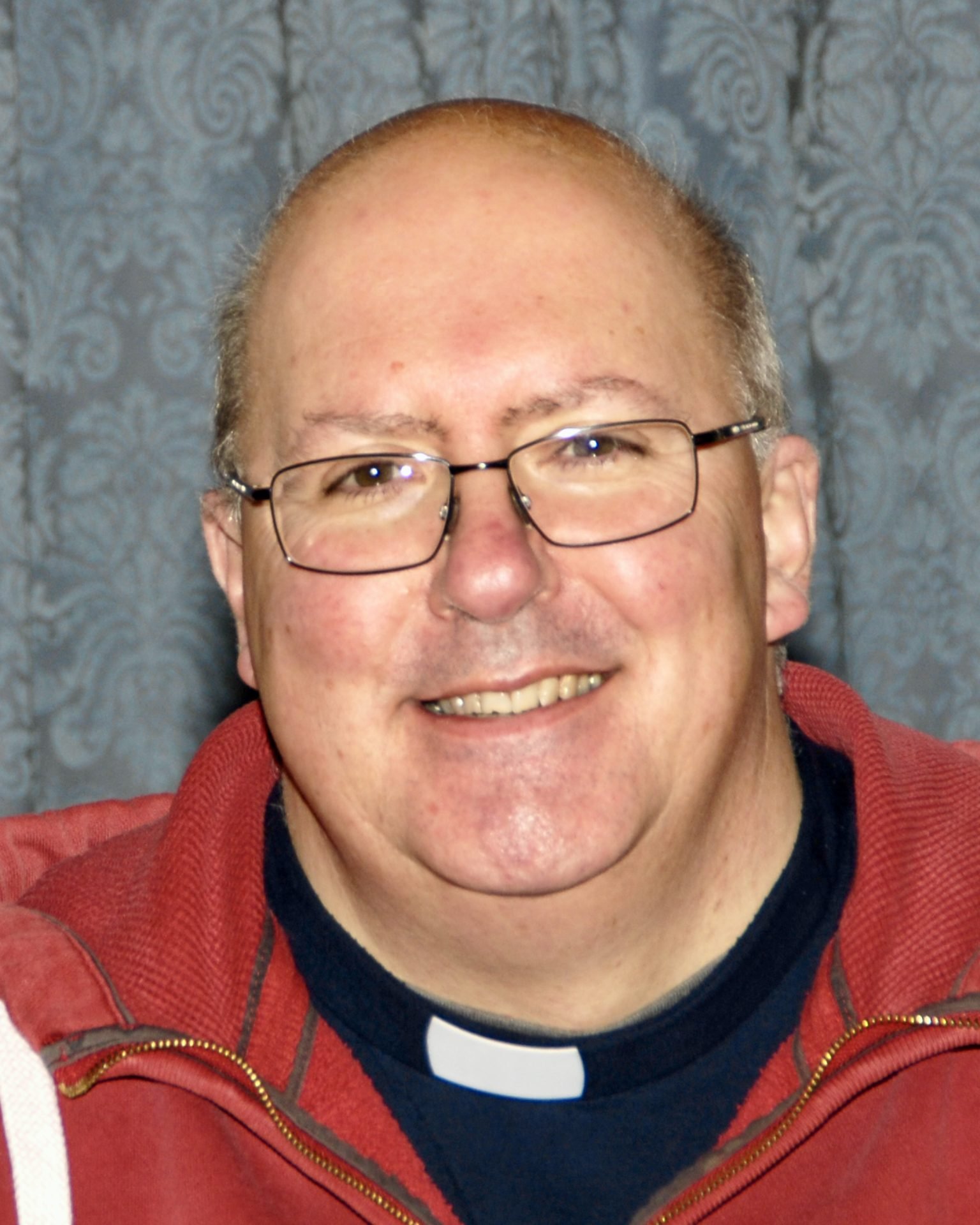 Jonathan Widdess, a man wearing glasses and a clerical collar, smiles warmly.