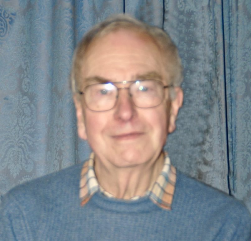 Chris Webb, a man wearing glasses and a blue sweater, smiles gently.