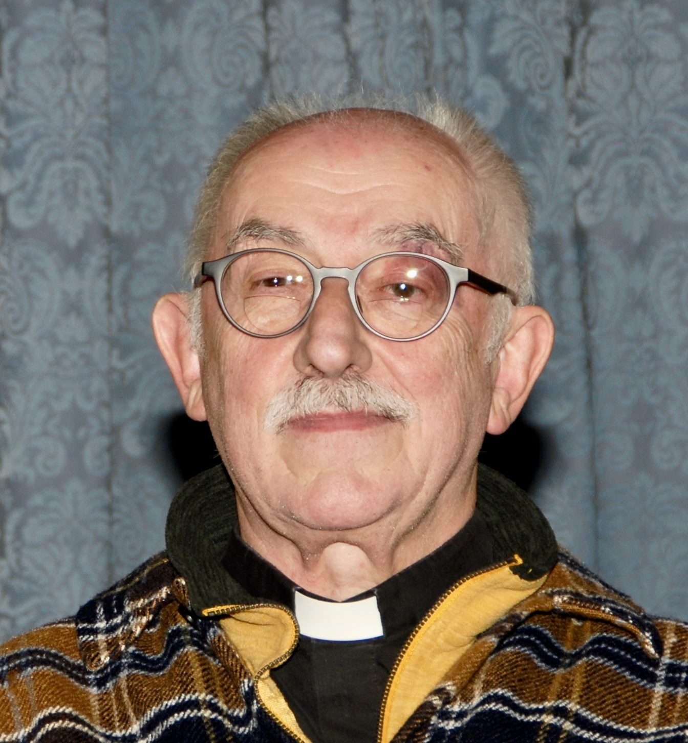 Michael Cluett wearing glasses and a clerical collar, smiling.