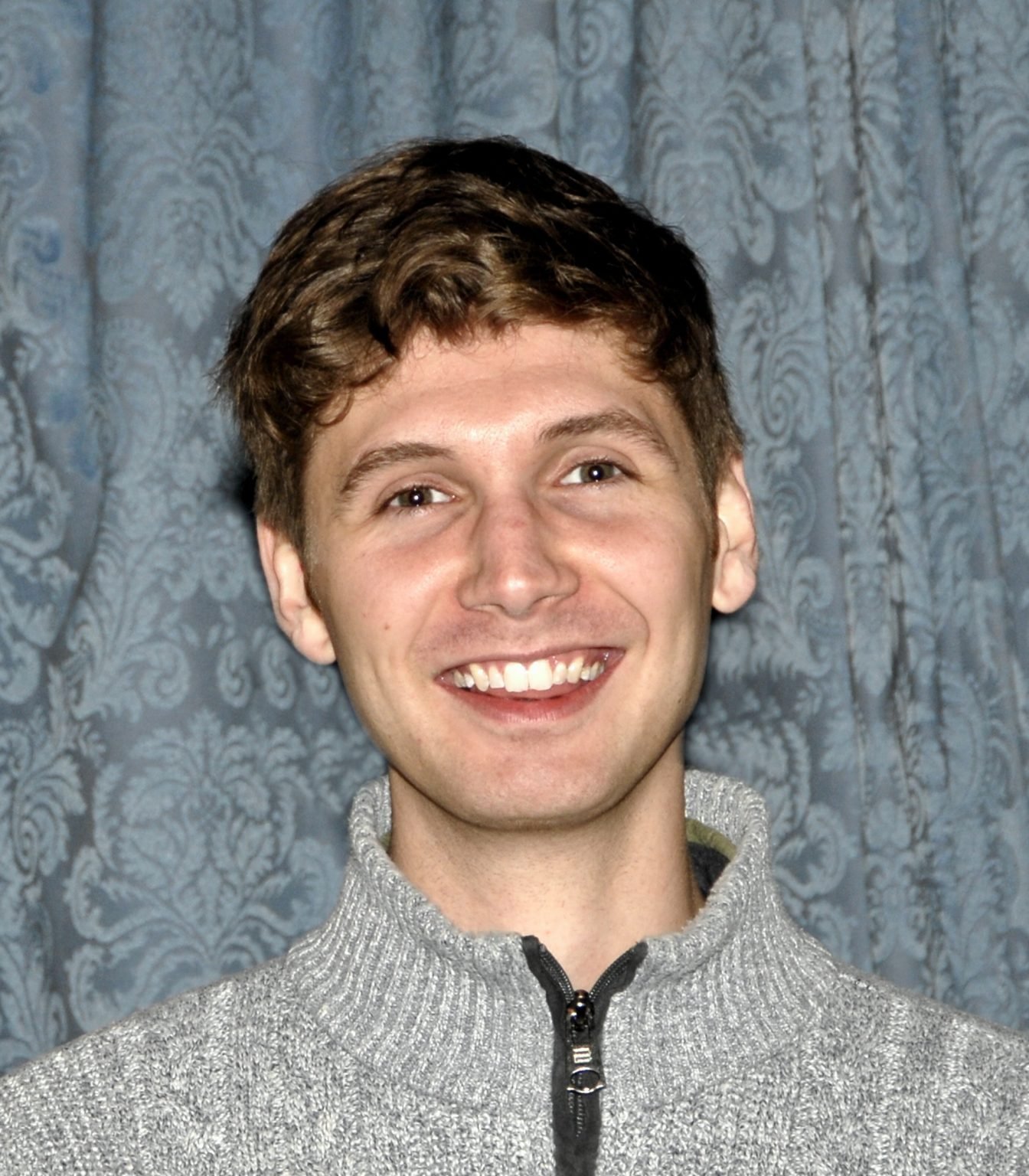 Ewan Murray smiles at the camera in a grey sweater.