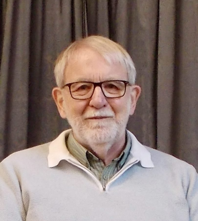 Stuart Vince, a white-haired man with glasses and a beard, wearing a light blue sweater.