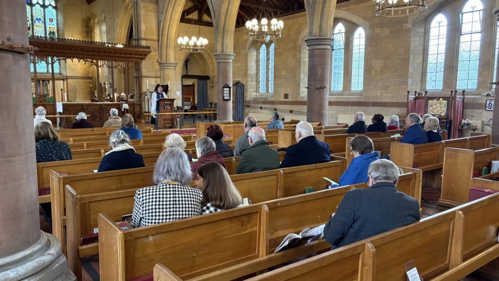 Congregation seated in a church during a service, with a person at the lectern.