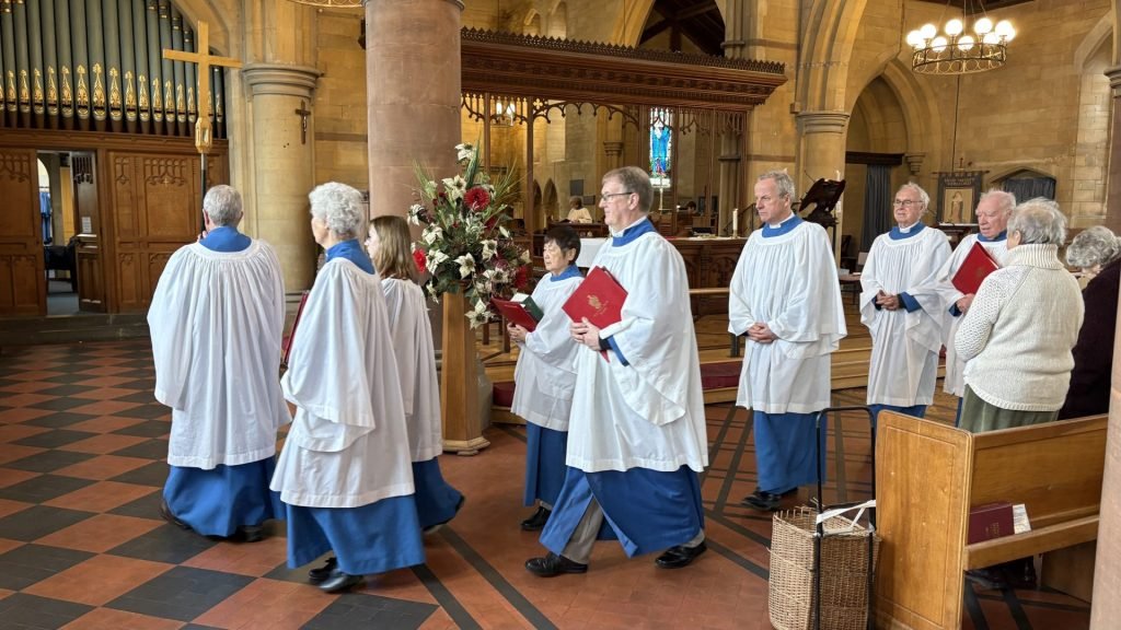 Choir members in robes process through a church, holding hymnals.