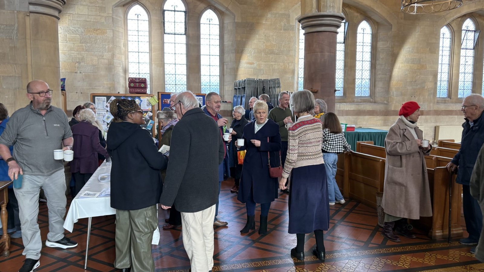 People mingling and chatting in a church hall with a coffee urn and table