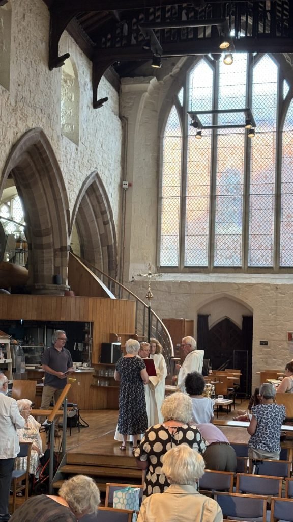 A worship service in a church with stained glass windows and attendees.