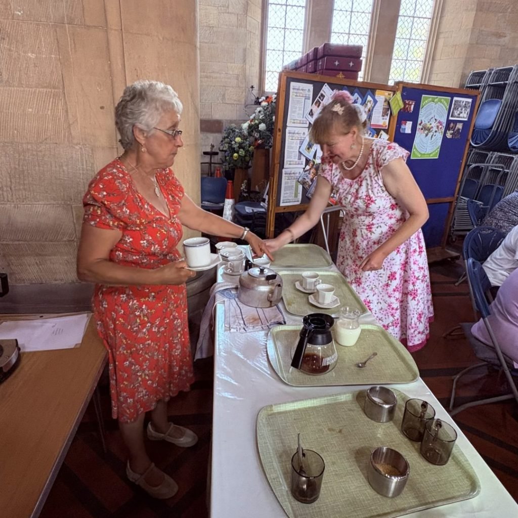 Two women serving tea and coffee at a CHATT event in a church hall.