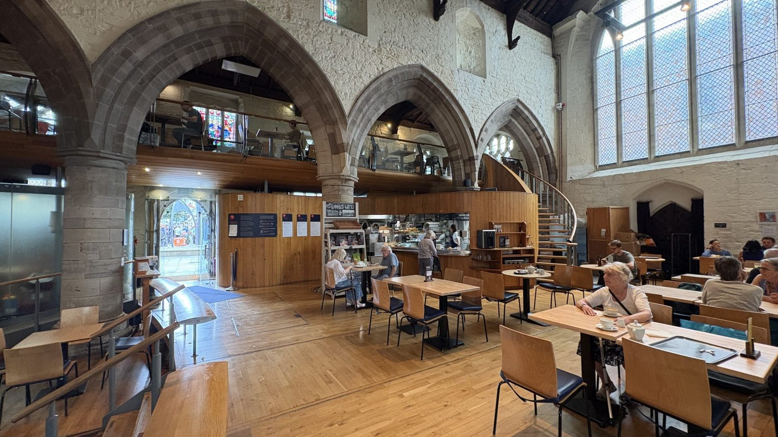 Interior of a converted church cafe with arched windows and wooden tables.