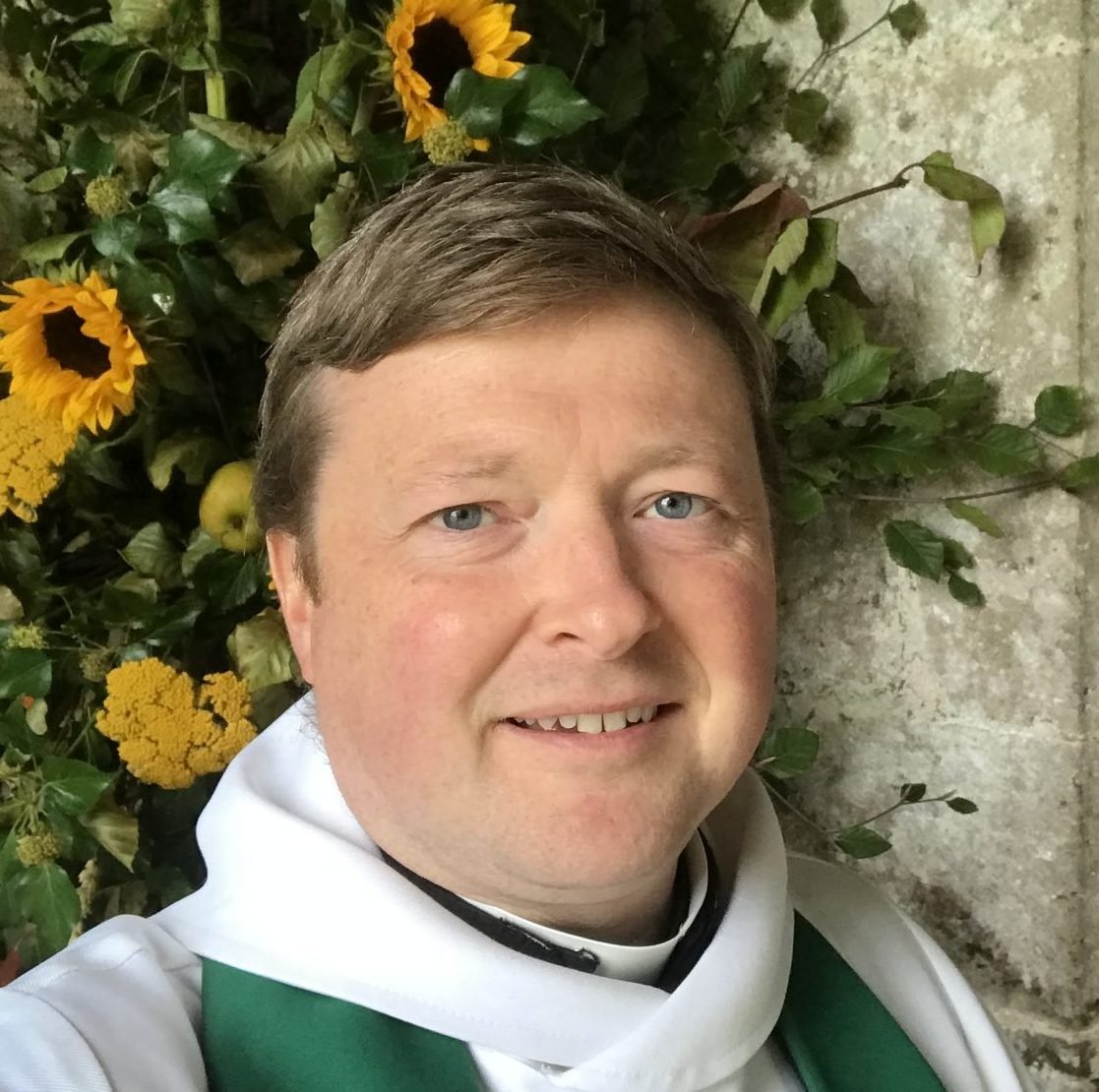 Paul Roberts in clerical attire with sunflowers and greenery
