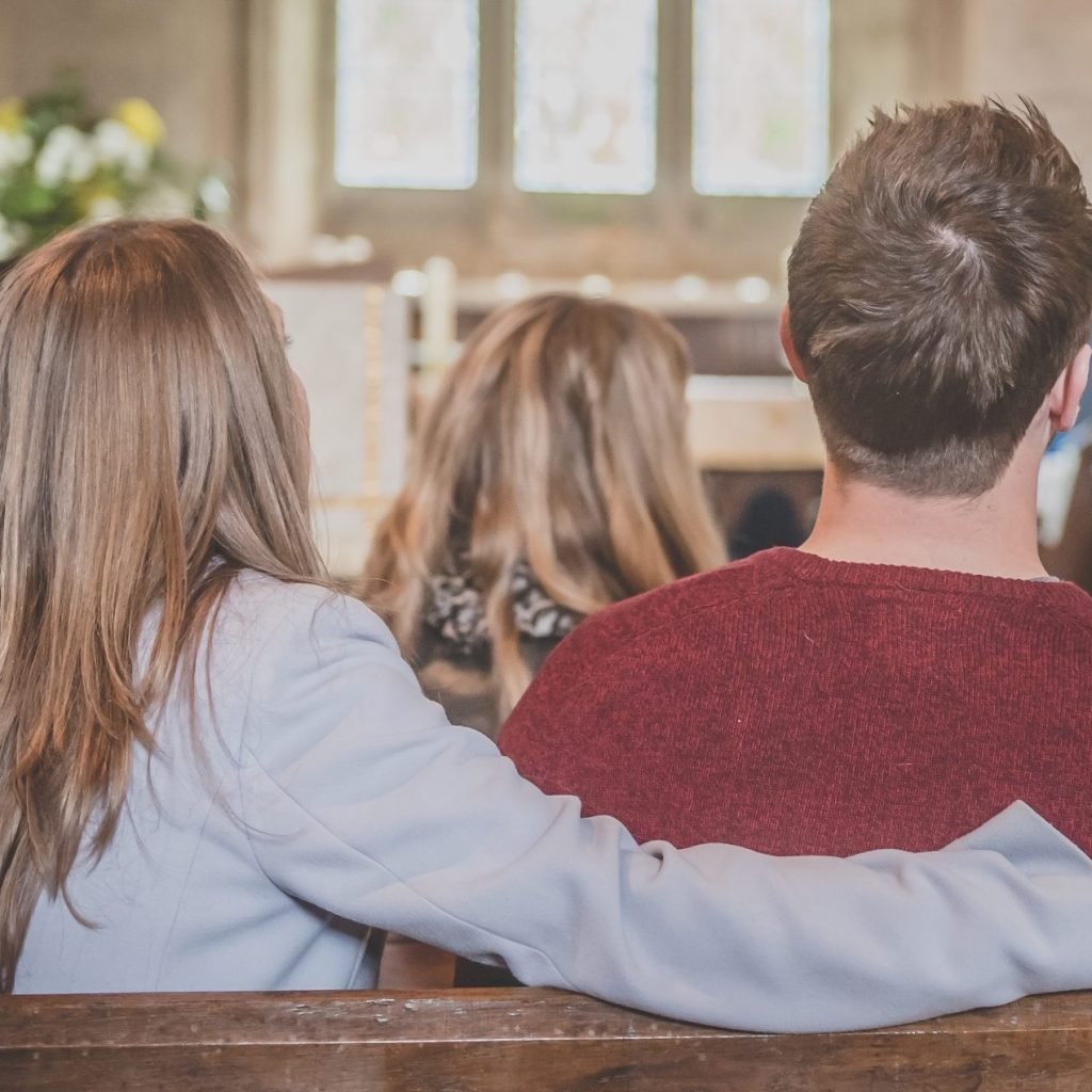 Couple in church pew, woman's arm around man, during wedding banns announcement.