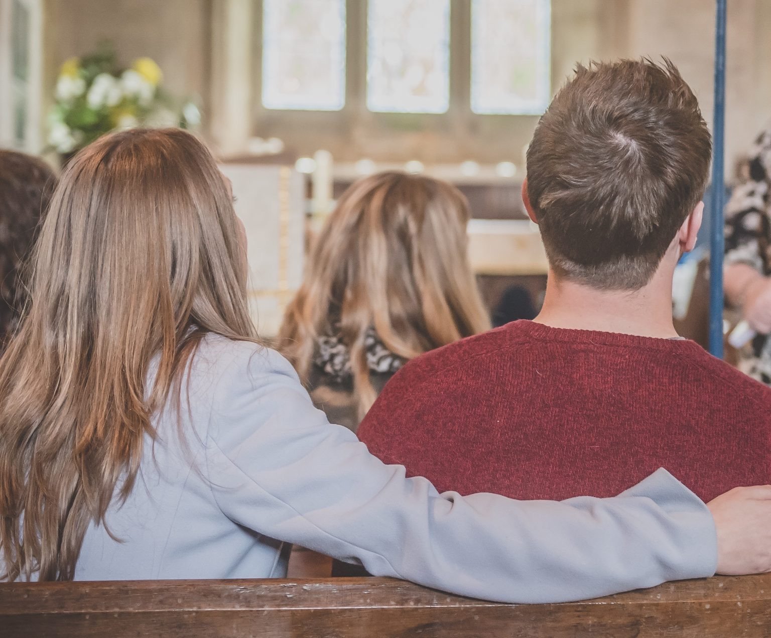 Couple in church pew, woman's arm around man, during wedding banns announcement.