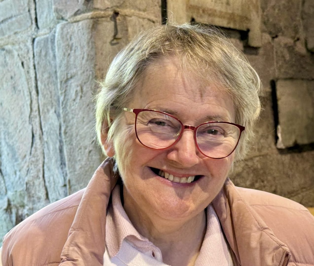 Diane Bates smiling, wearing glasses and a pink jacket.