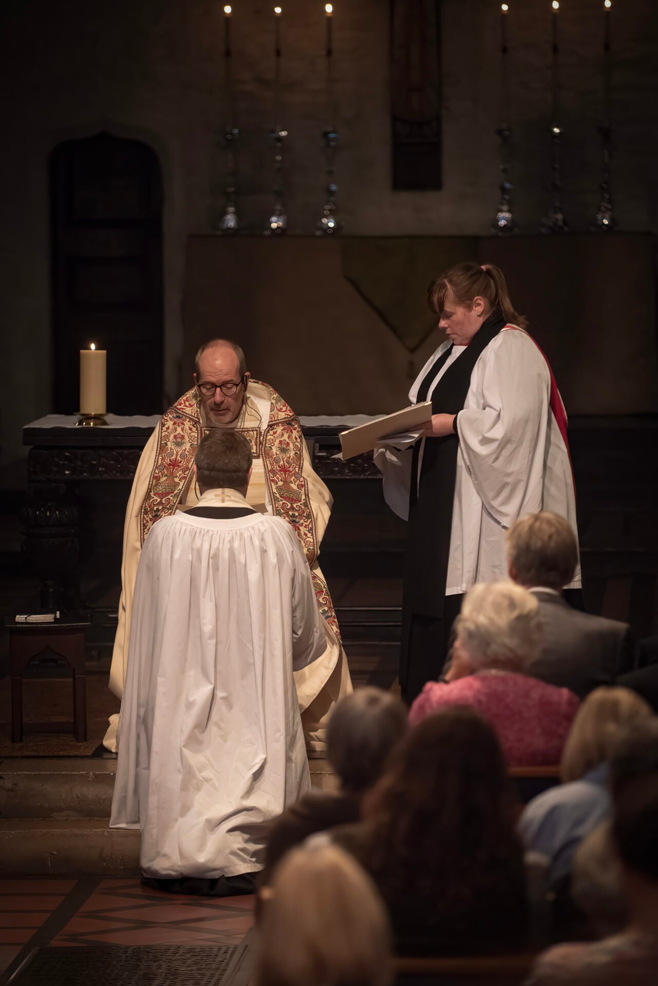 Paul Roberts kneels in front of Bishop Richard, while Jane, the Bishops Chaplain looks on